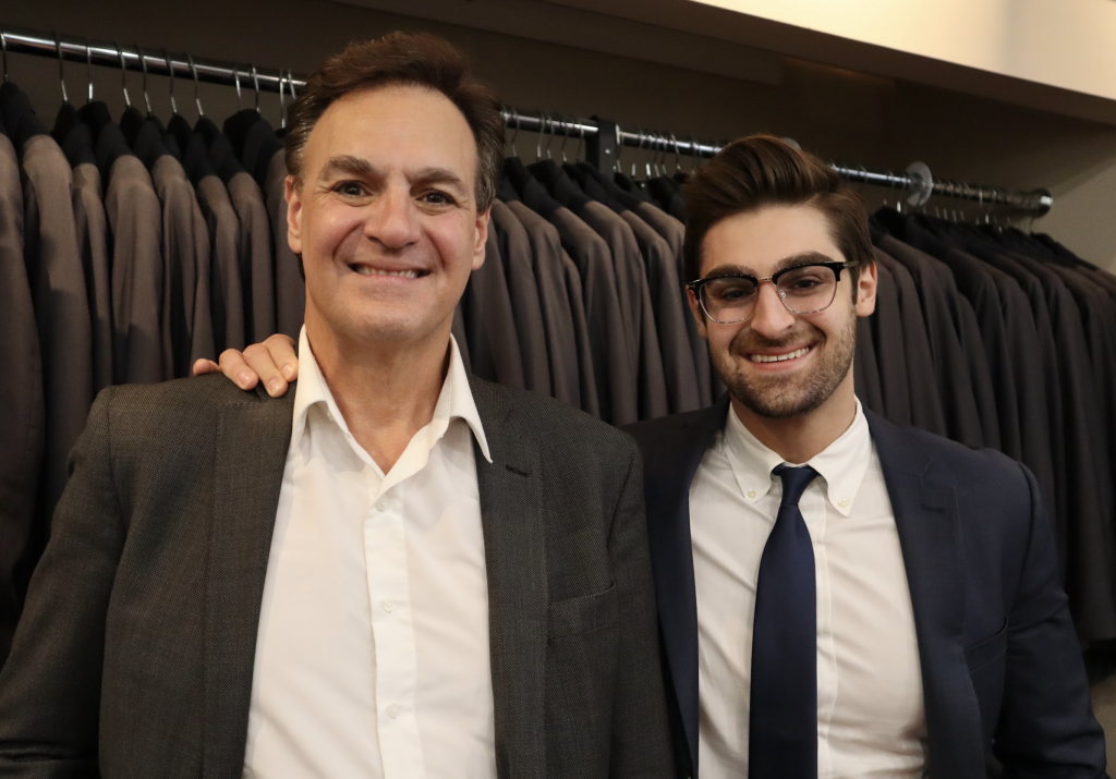 Samuel Feldberg and Joseph Feldberg pose for a photograph next to a rack of suits.