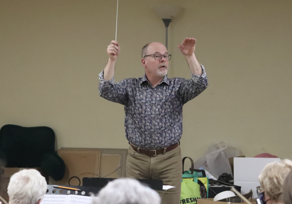 A man in a flashy gray shirt conducts an orchestra 