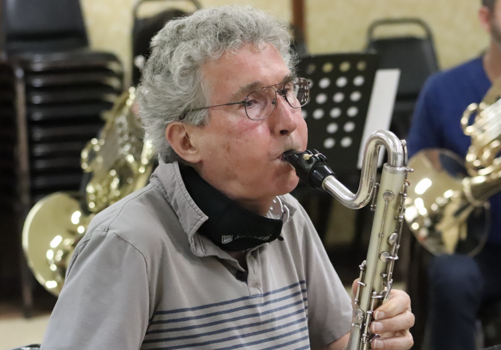 A man in a gray shirt blows on a bass clarinet