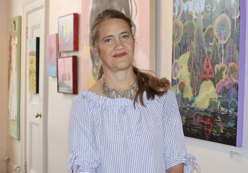 Ingrid poses for a photo in the art gallery. Art work is on display behind her.