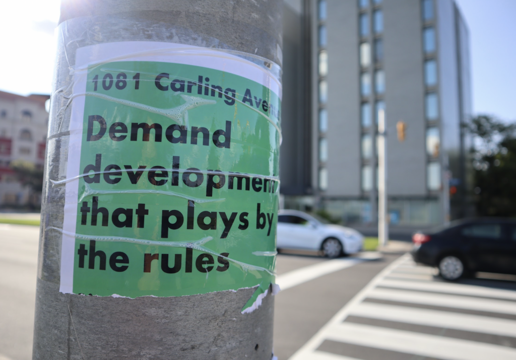 A sigh reads “demand development that plays by the rules.” It’s taped to a post outside 1081 Carling.