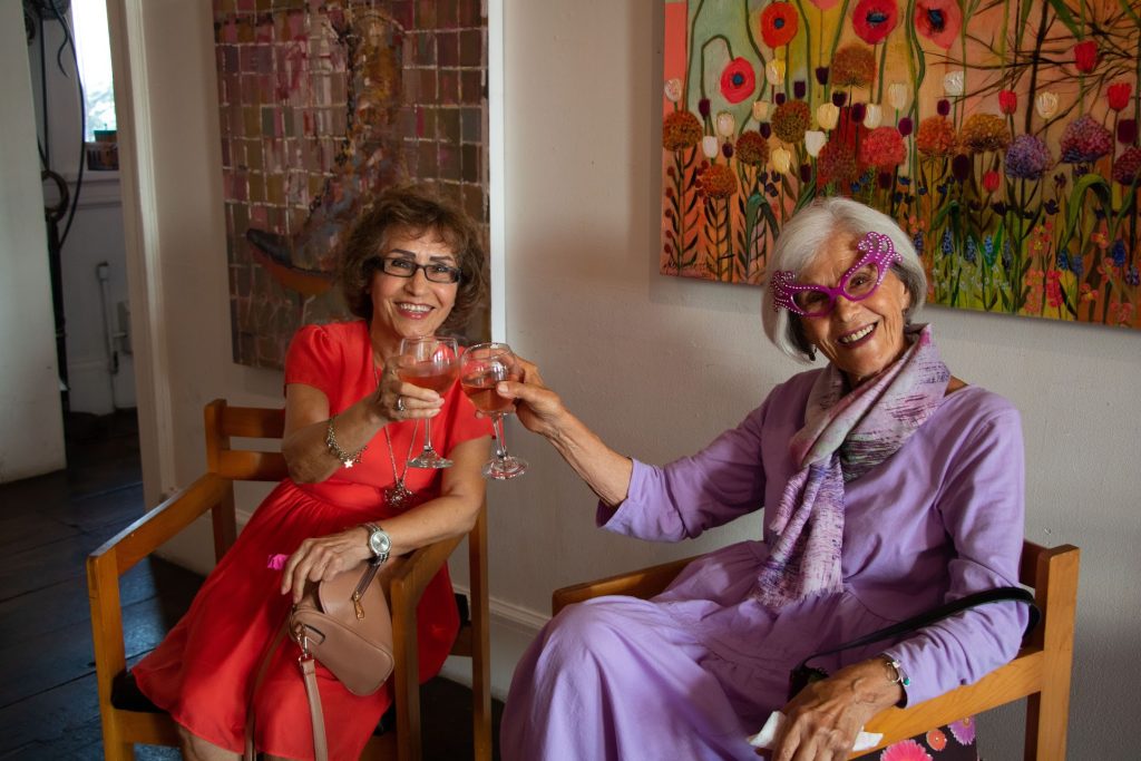 Two women holding up glasses of wine pose for a photo.