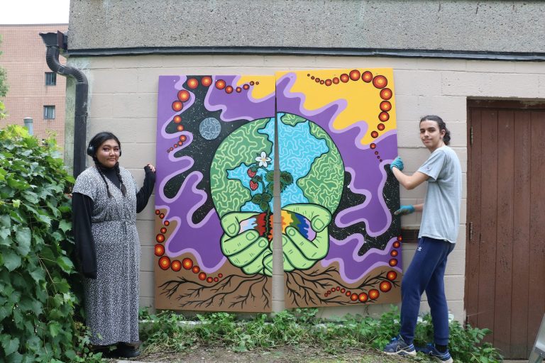 Two people stand next to a colourful mural.