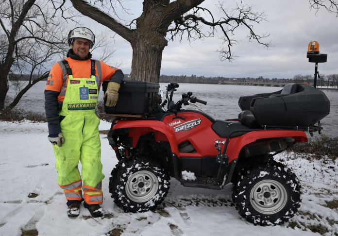 A man wearing a bright orange shirt and bright green winter overalls poses for a photo with his red ATV