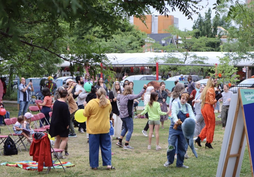 A group of people stand and dance in Parkdale Park. 