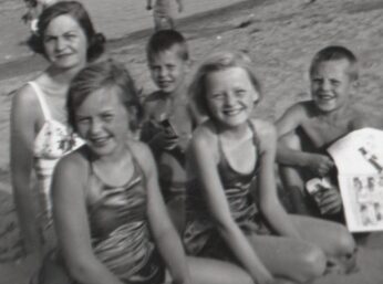 A black and white photo of five kids on a beach. 