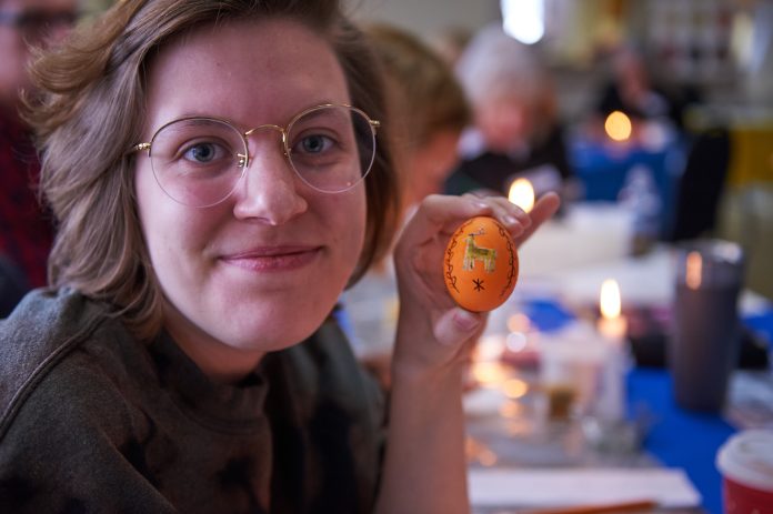 A girl wearing glasses holds up an orange coloured painted Easter egg