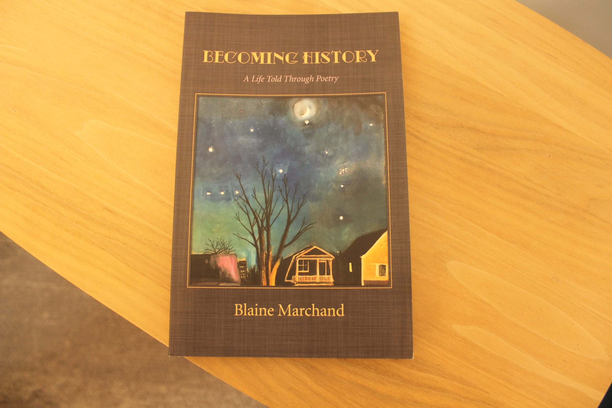 A picture of the book sitting on a table. The cover has a painting of a night sky with some houses, a tree, and the moon.