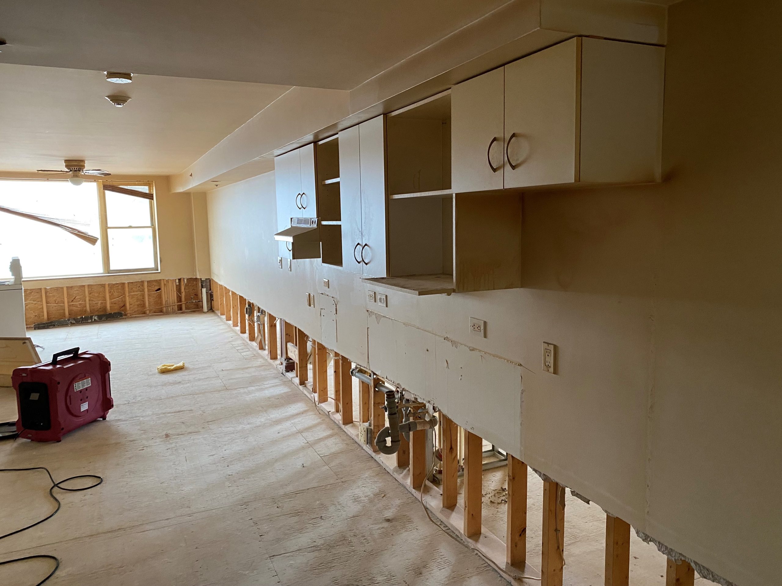 A photo showing the lower part of walls and flooring removed. The upper walls and cabinets are still in the room.