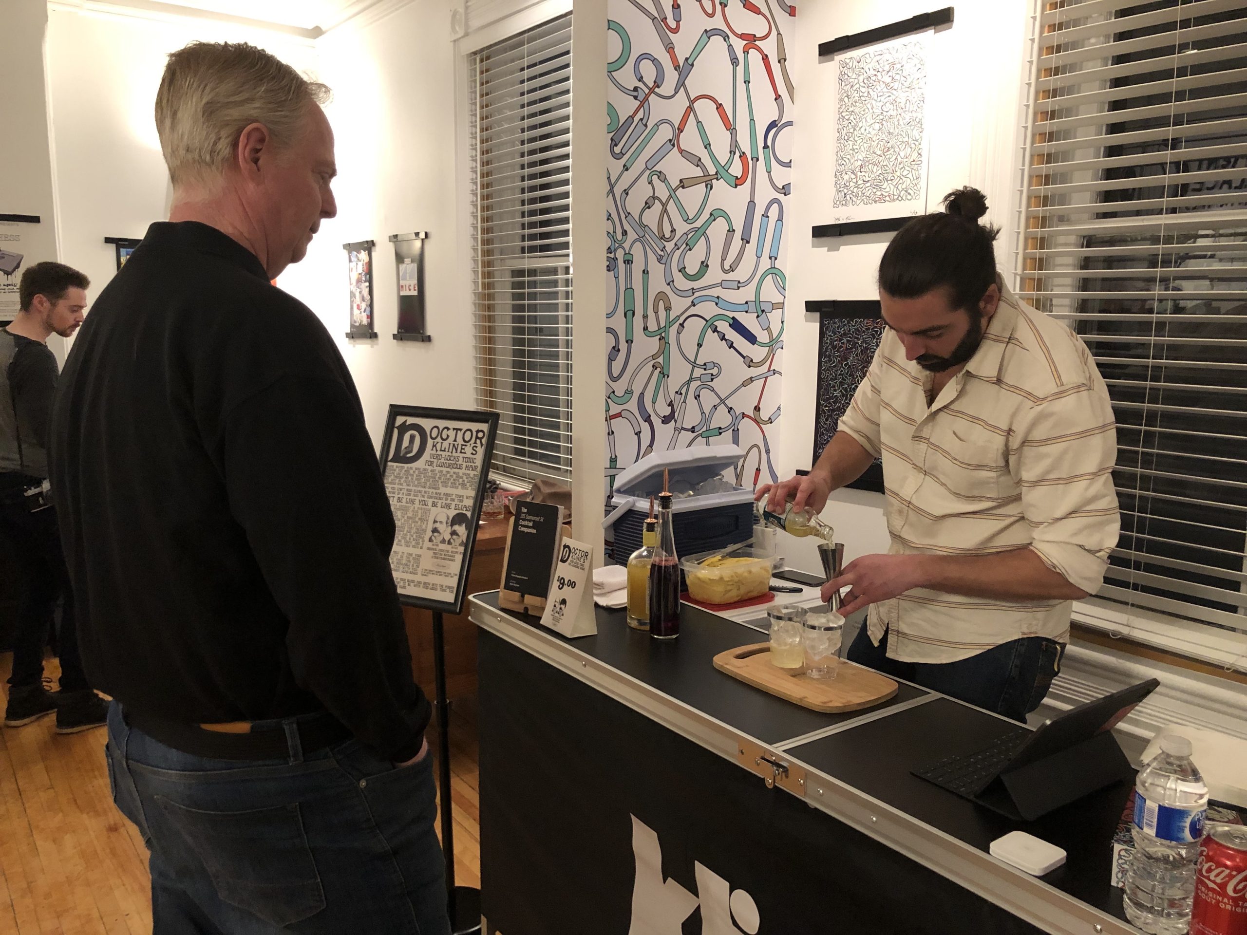 A bartender pours a drink for a man who is standing nearby.