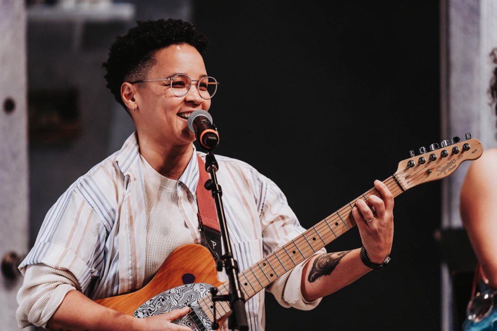 Kimberley holds a guitar on stage while singing. 