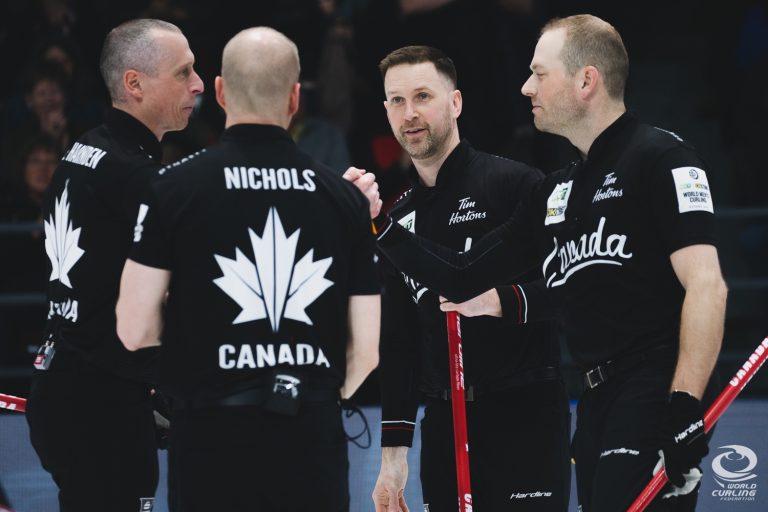 Four curlers from team Canada chat together on the ice.