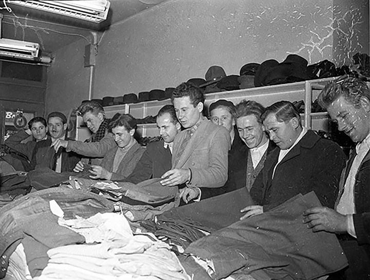 An old black and white photo of multiple refugees receiving clothing. They are smiling and happy.