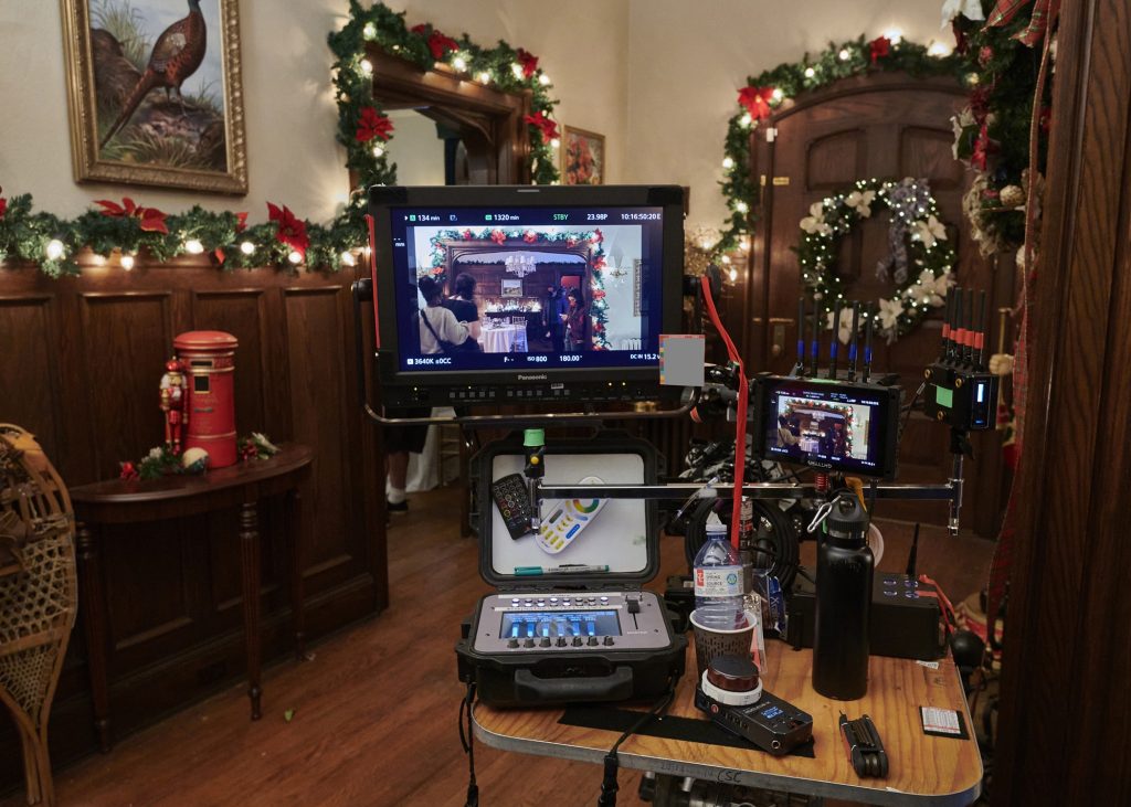 A house is decorated with garland and white lights for Christmas. Filming equipment is in the middle of the house.