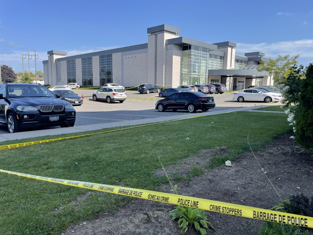 Police tape lines a convention centre with cars parked in a parking lot. 