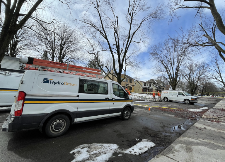 Hydro Ottawa trucks are parked in the middle of the street as hydro crews survey the damage. Police tape prevents access to the street.