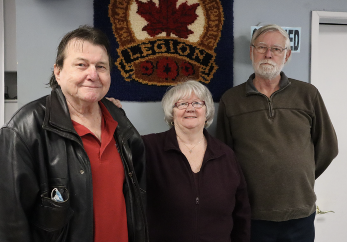 Three people pose for a photograph in front of a wall.