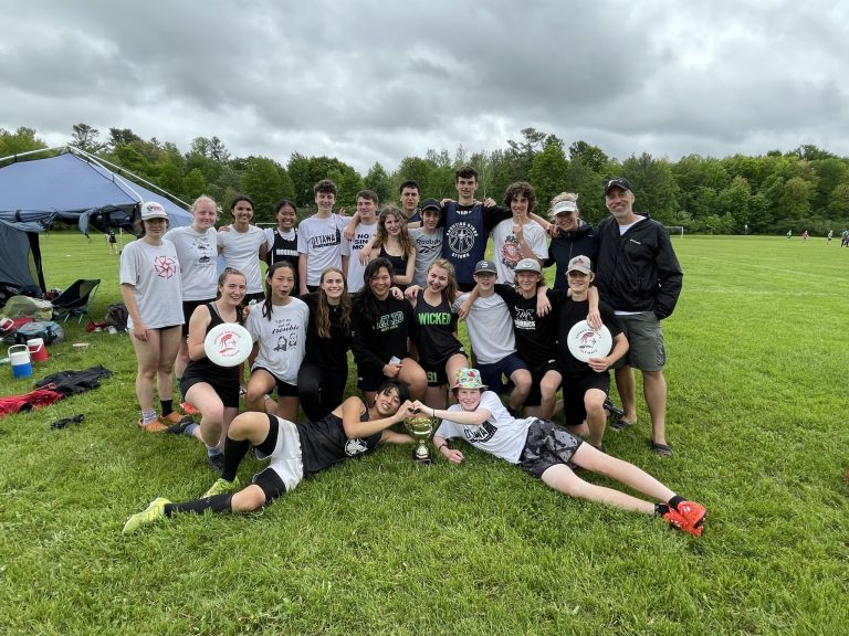 A group of students pose for a photo on a field. The sky is grey.