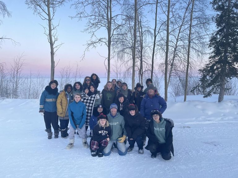 Students from Notre Dame High School pose for a photograph as the sun is setting behind them. There is snow on the ground.