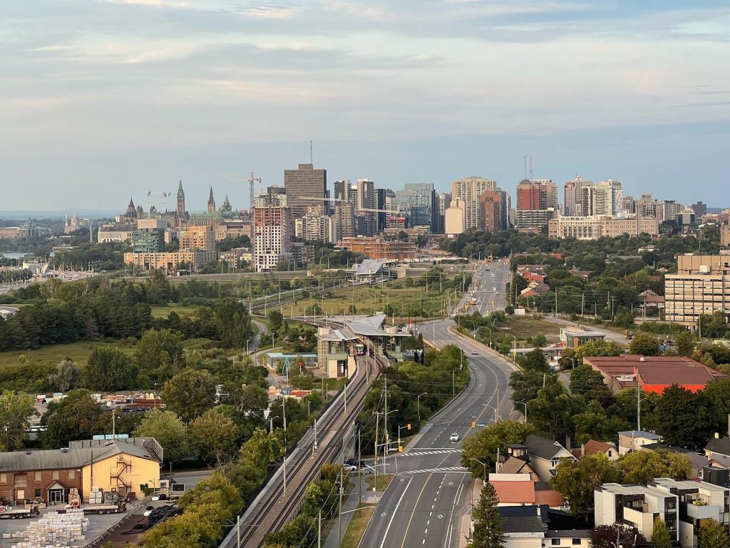 The Ottawa skyline on a bright sunny day. Parliament Hill can be seen alongside large office towers and the Bayview LRT Station. 