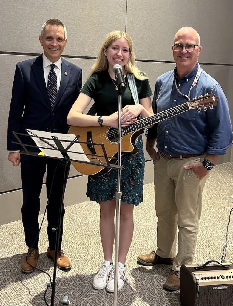 Three people pose for a photograph. The girl in the middle is holding a guitar. 