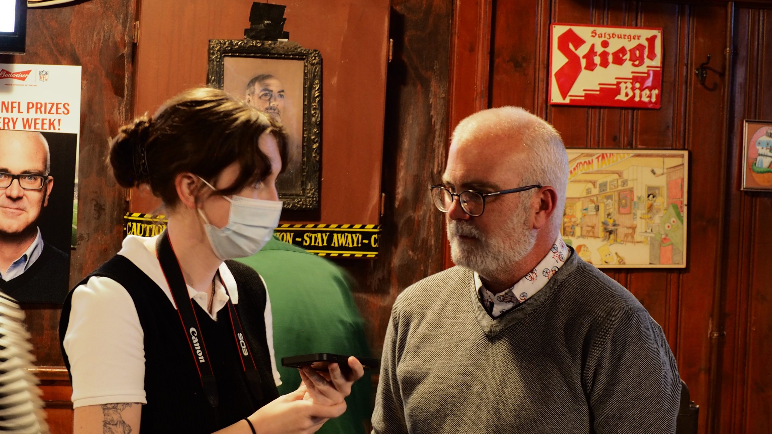 Emma, who is wearing a mask, interviews Jeff Leiper. 