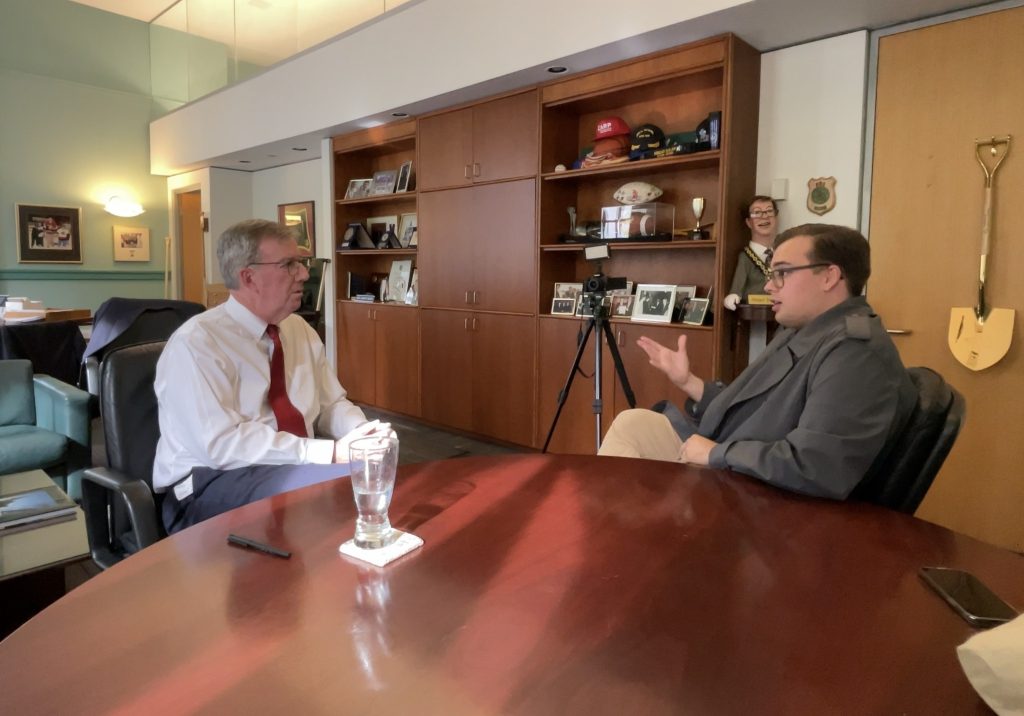 Charlie sits down at a board room table with Jim Watson. They are in the mayors office at Ottawa city hall. 