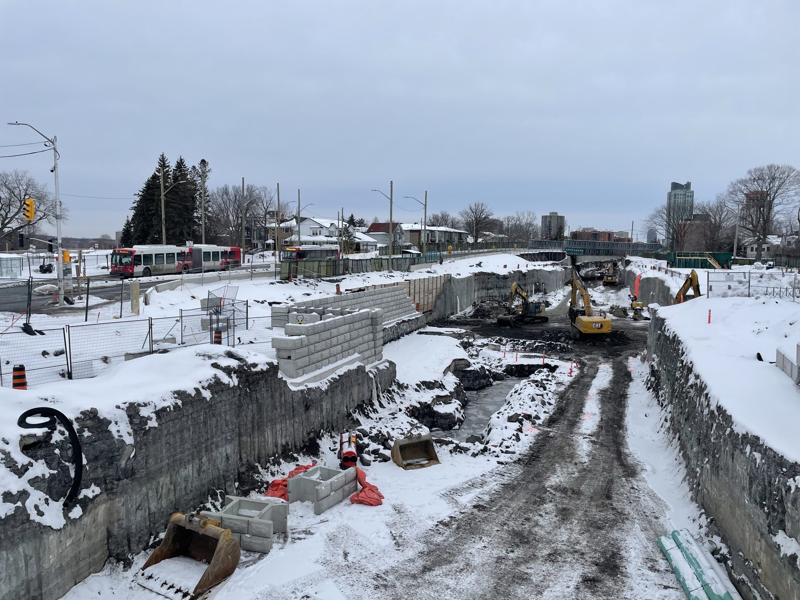 The construction pit outside of Dominion Station in Westboro. Construction machinery is working on the LRT line as a bus passes by on the left side.