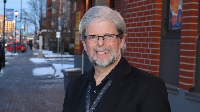 Dennis poses for a photograph outside the Wellington West BIA office. It’s winter and the sun is setting.