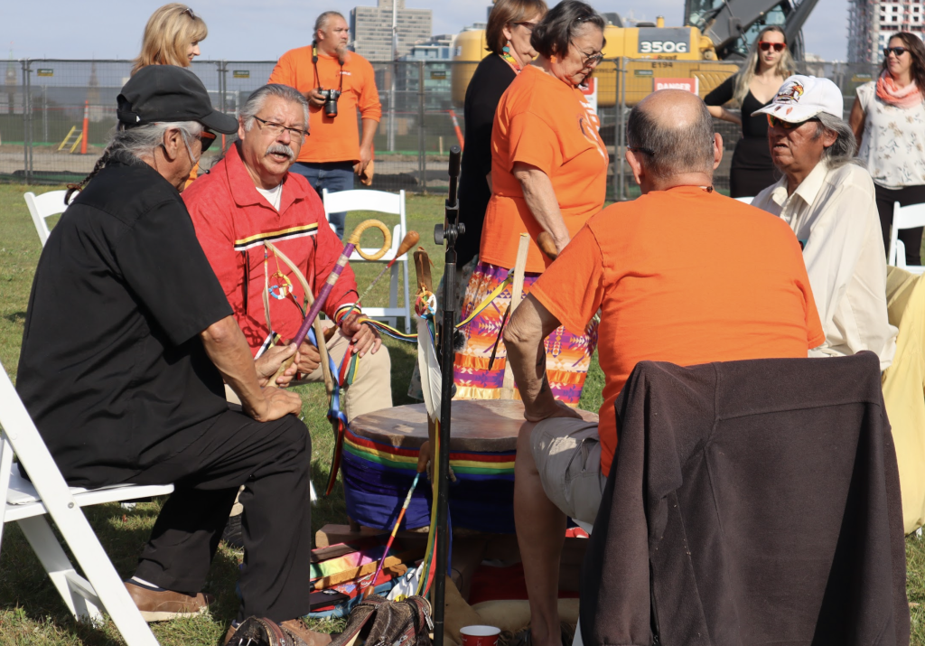 Four men beat on a drum with sticks. 