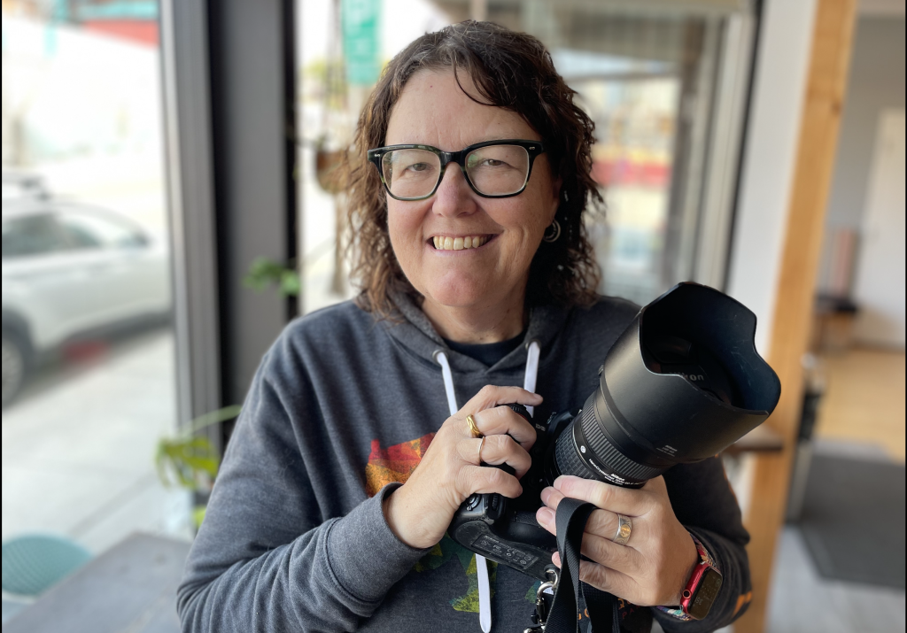 Ellen smiles as she poses for a photograph holding her camera. 