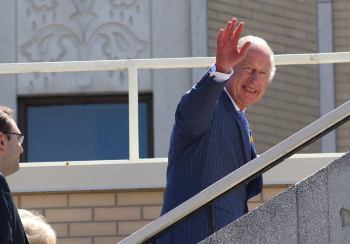 Prince Charles smiles and waves to the camera as he walks up the outside stairs of the Ukrainian Church.