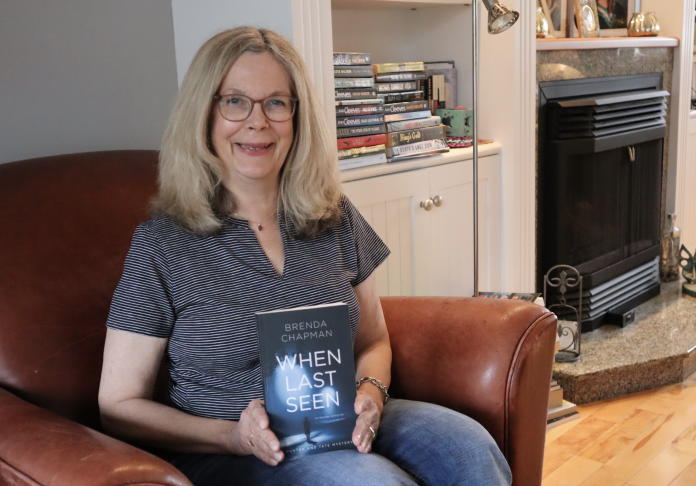 Brenda sits down in a chair and smiles as she poses for a photograph with her book When Last Seen.