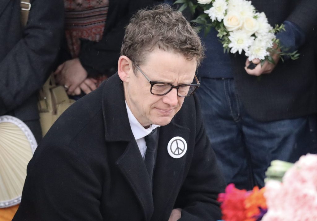 Joel Harden wears a peace button as he kneels down to lay flowers. 