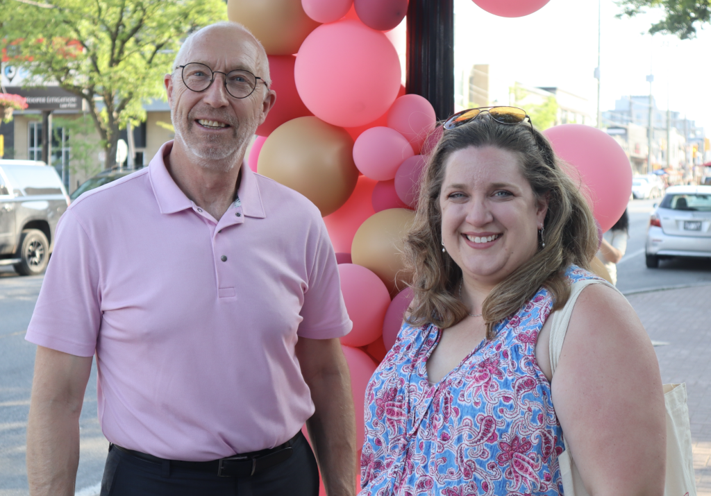 Rick and Judy pose for a photo on Richmond Road. Pink balloons are on a clock pole behind them.