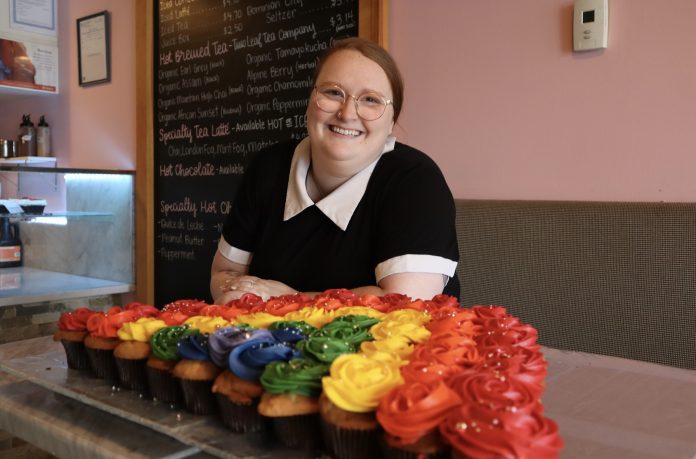 Laura poses for a photograph with a display of colourful cupcakes