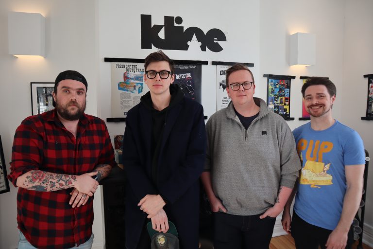 Four men pose for a photograph in front of the Kline logo.