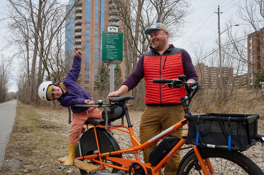 A child playfully plays on a bike with his dad watching. 