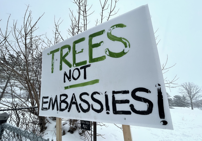 A sign reading “trees not embassies” sits at the entrance to the park.