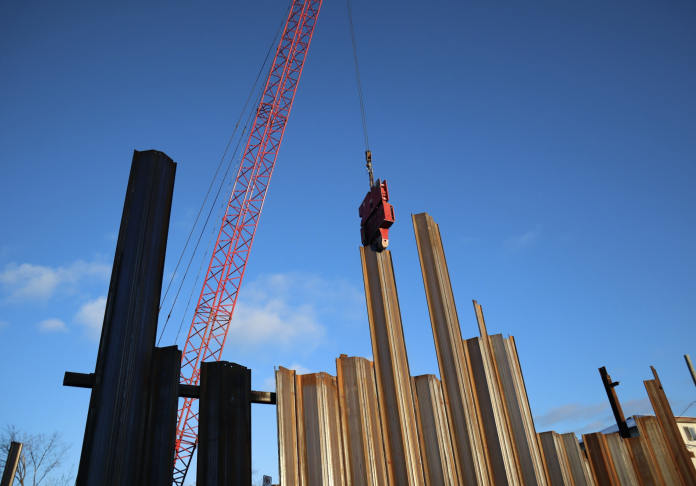 A red crane bangs in pieces of metal at a construction site.