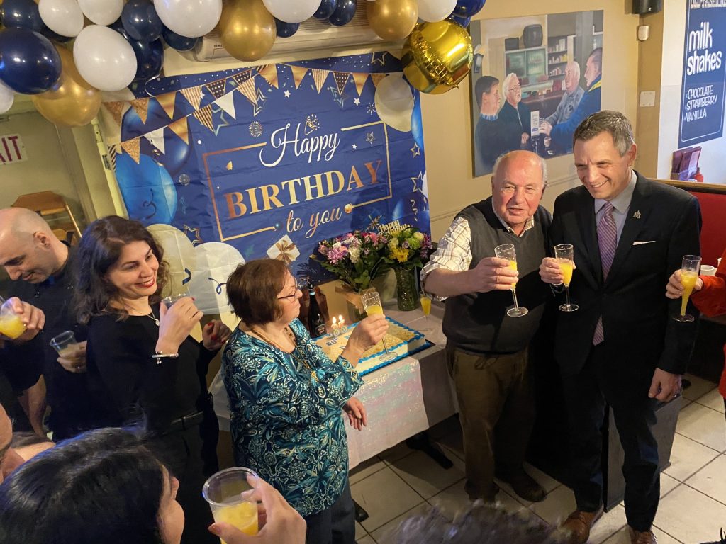 John and mayor mark Sutcliffe raise a glass of orange juice. Others are watching. 