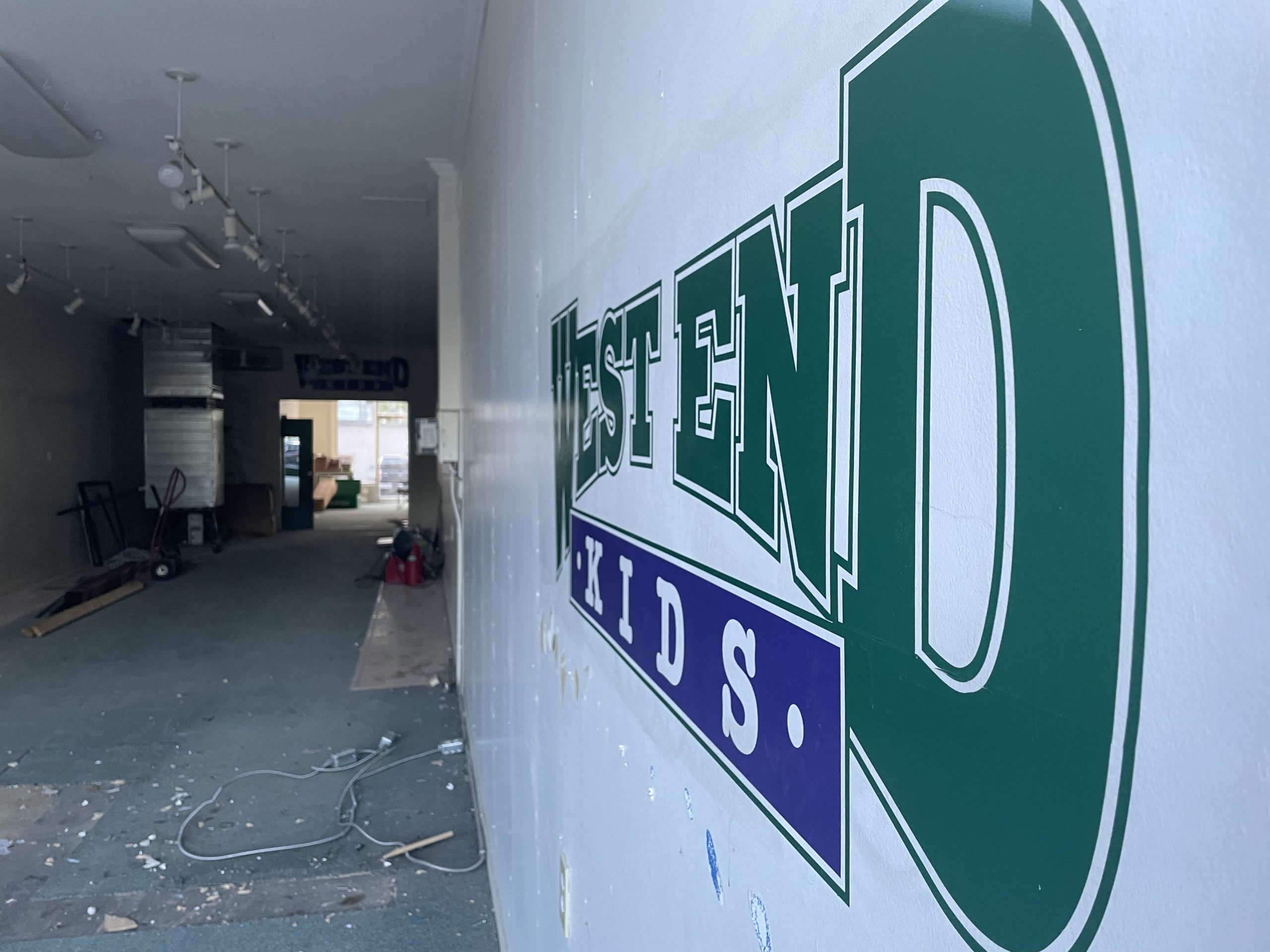 The inside of West End Kids is empty besides a ladder in the distance. The stores logo is seen on the right wall.