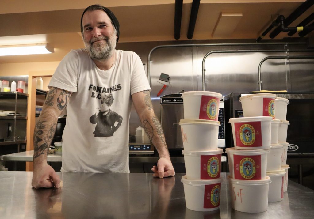 Tim poses for a photograph in a kitchen next to pints of his ice cream.