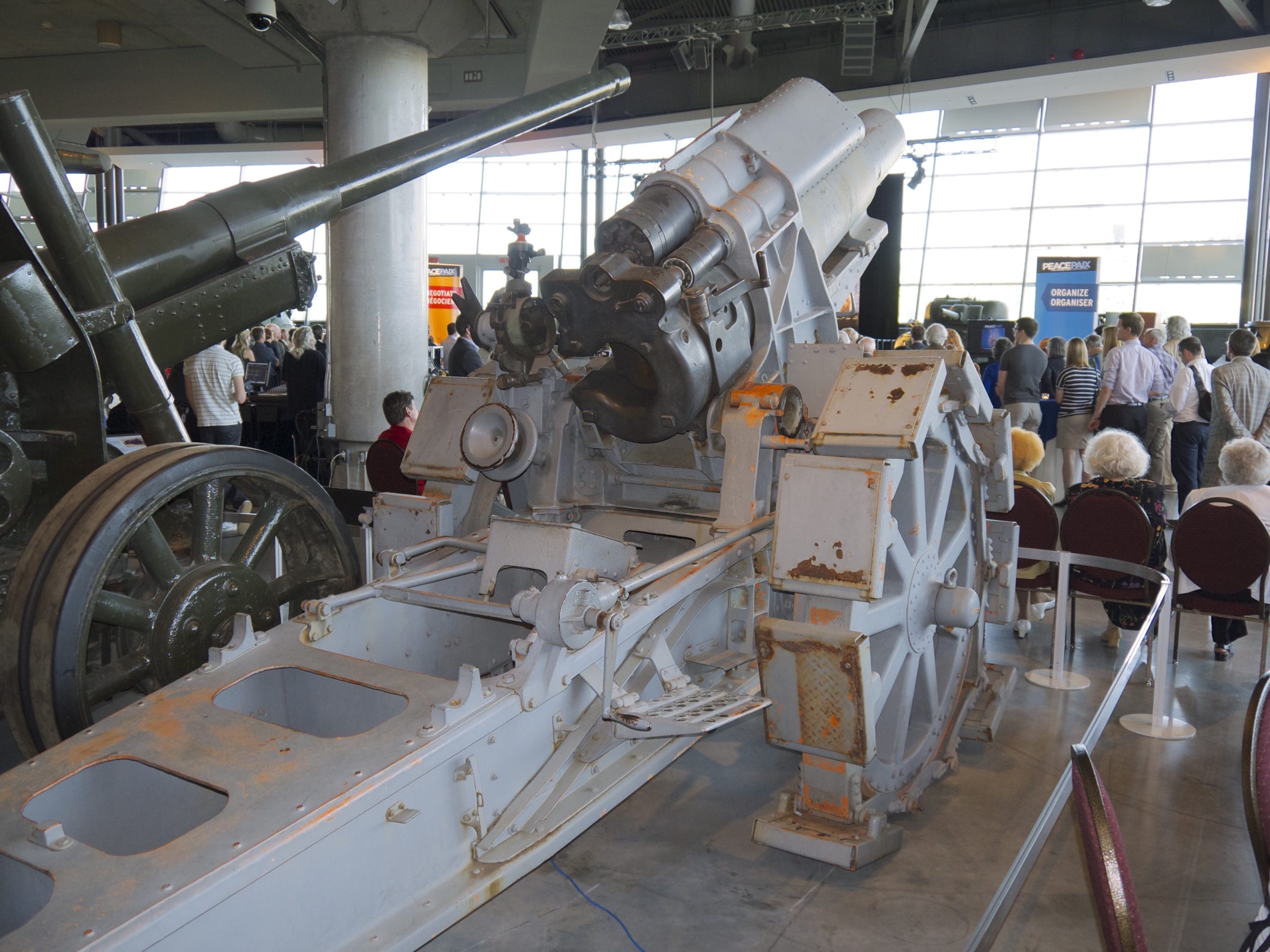 A howitzer on display at the war museum in Ottawa. People can be seen mingling at a function in the background. 