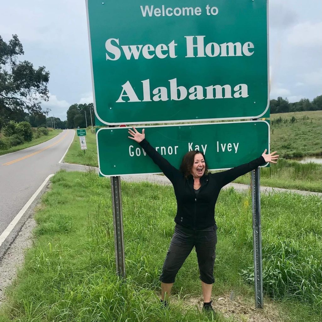 Sherri standing beside a sign reading “Sweet Home Alabama.”