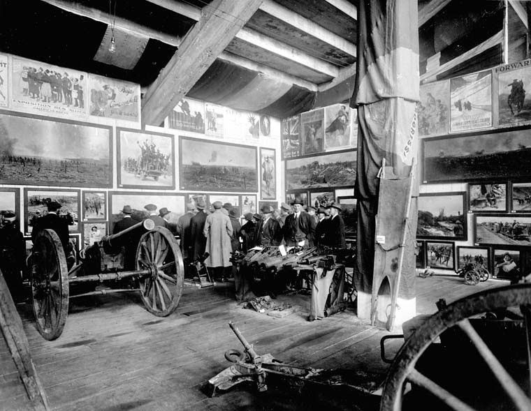 An old black and white photo showing a number of people looking at old war memorabilia.