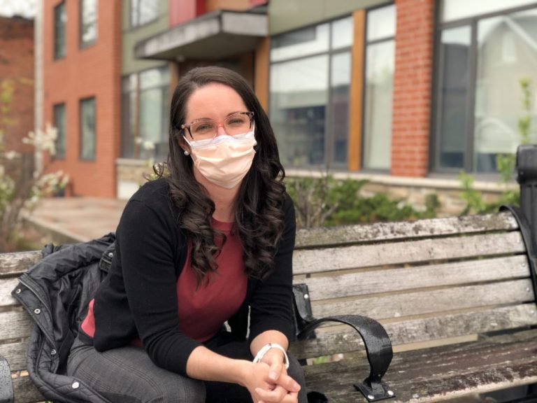 Sarah Davis sits on a wooden park bench in front of a row of brick buildings in Ottawa