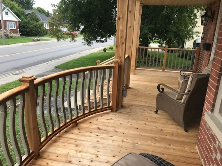 A wooden porch in Ottawa is seen with two chairs on it looking out onto a street