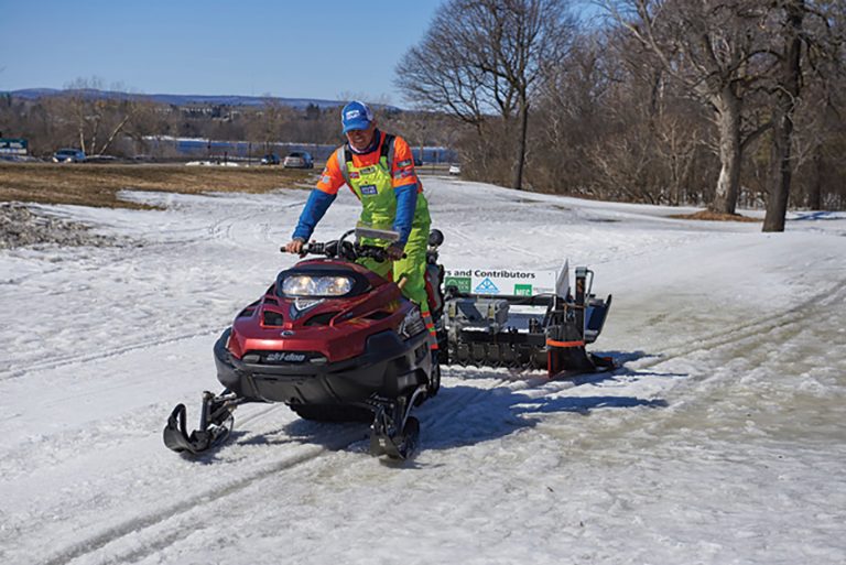 Dave Adams driving a snowmobile on the SJAM trail on a sunny winter day in 2017.