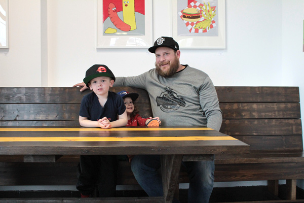 Hintonburger owner Thomas Williams sits with his sons Cecil, 4, and Cameron, 2, at one of the restaurant’s new tables made by Kemptville carpenter Larry Gorton. Photo by Jacob Hoytema